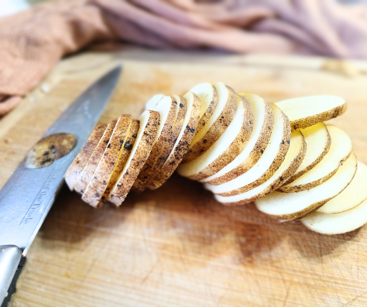 a potato sliced up not larger than 1/2 centimeter on a cutting board next to knife for soup