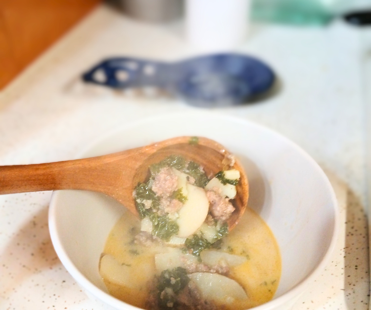 Zuppa Toscana soup in white bowl and wooden spoon.