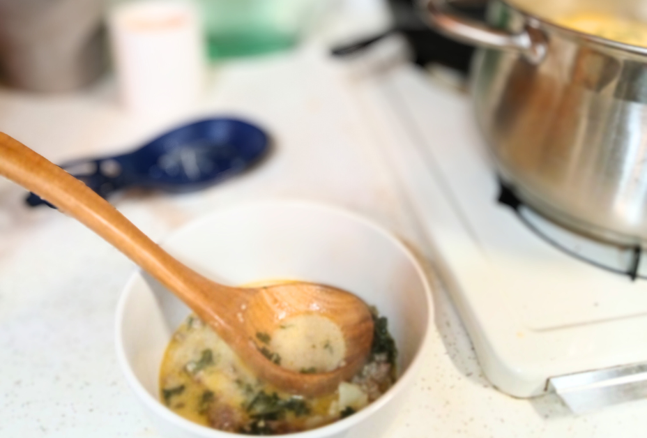 spoon in bowl with zuppa Toscana soup in it on the counter next to silver pot